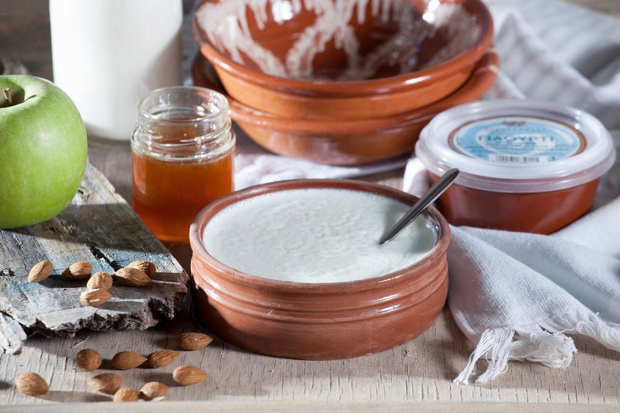 ceramic pot with 'Mystakelli Dairy' yogurt and a jar with honey and a green apple and unpeeled almonds
